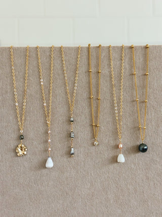 Set of gold necklaces with various pendants on a neutral background